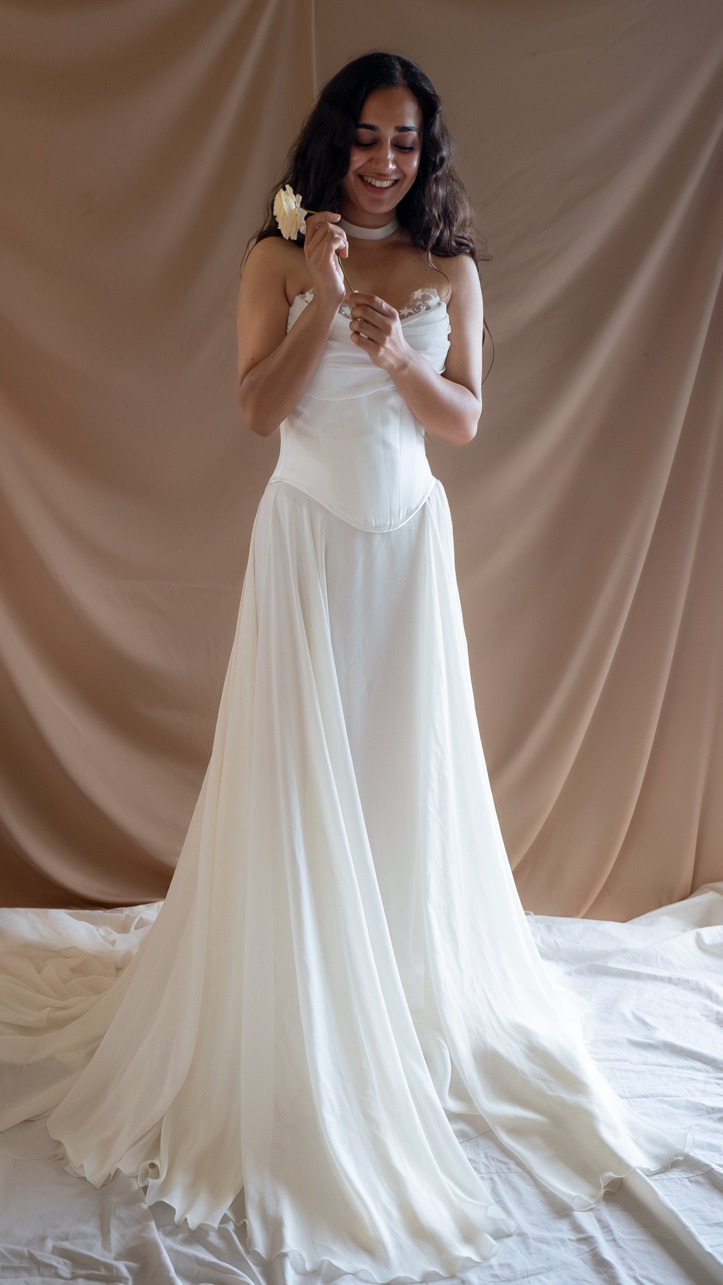 Woman in a fairytale vintage Basque waist wedding dress with a long train against a beige curtain backdrop