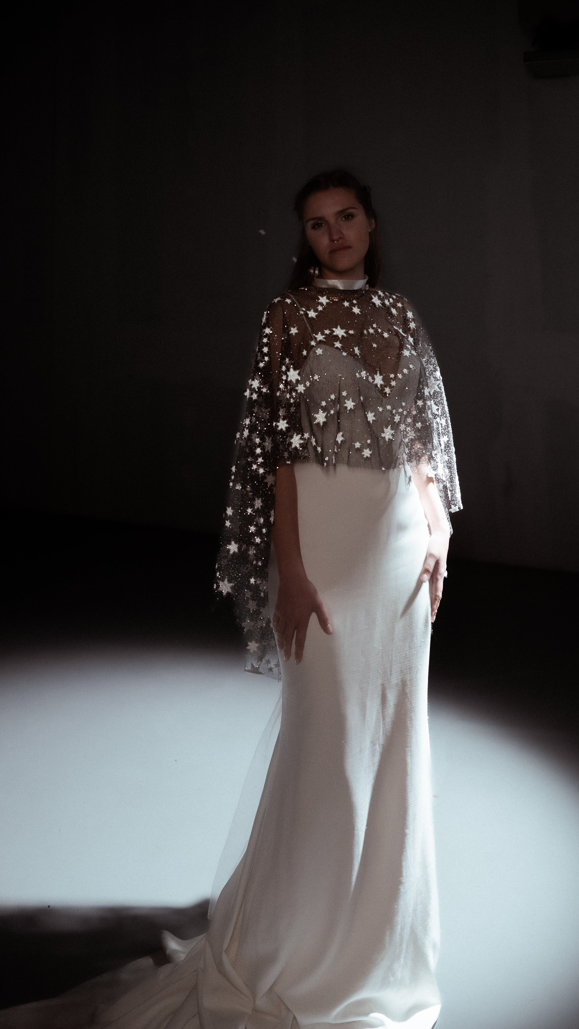 Woman wearing a white dress with a sheer overlay against a dark background