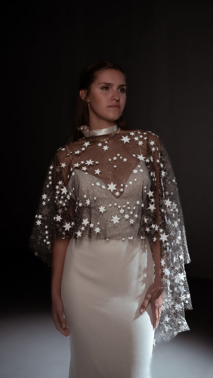 bride wearing a star-patterned cape over a white dress against a dark background