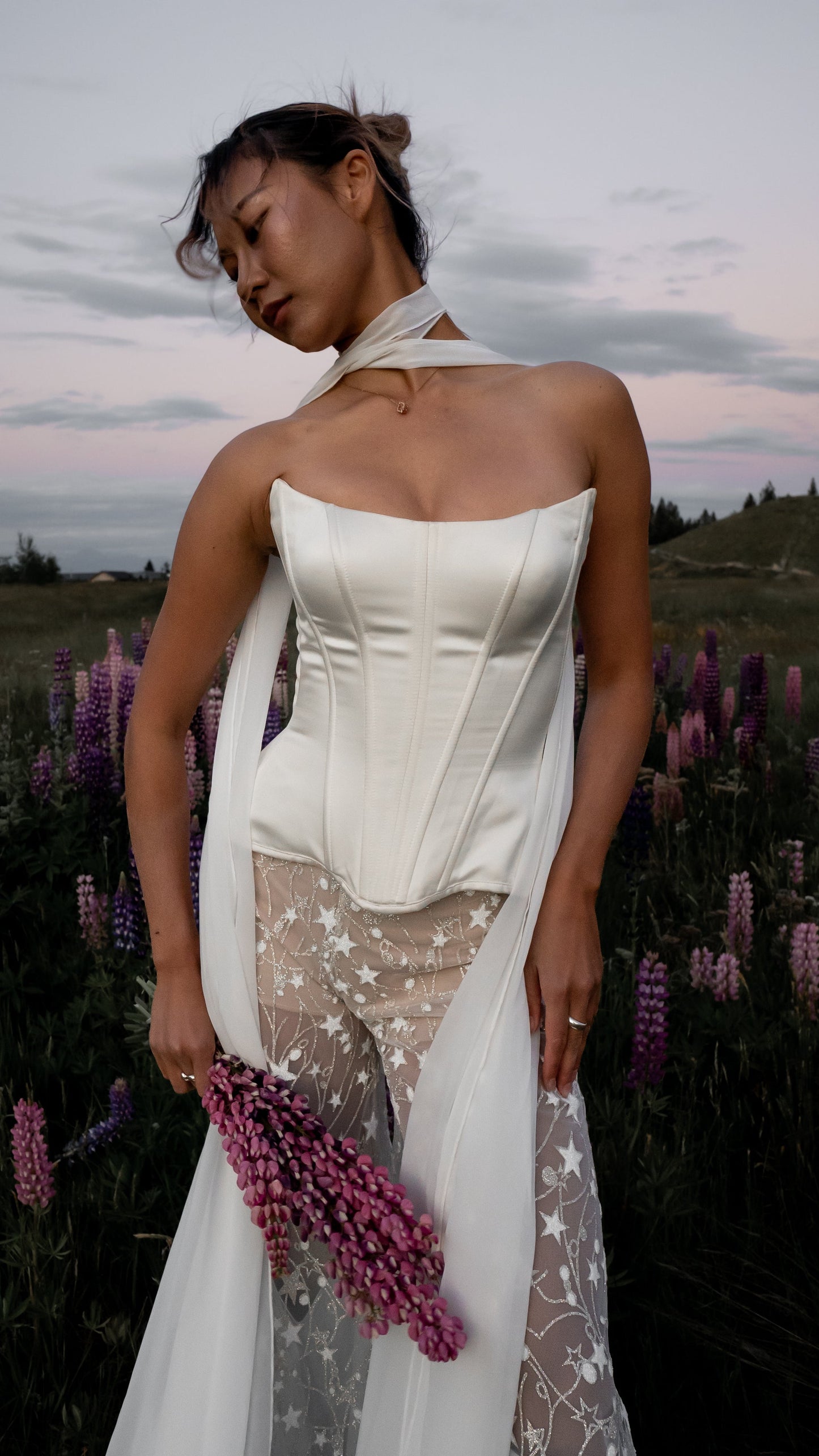 Bride in a white strapless Basque waist corset dress with star pattern pants standing in a field of purple flowers.