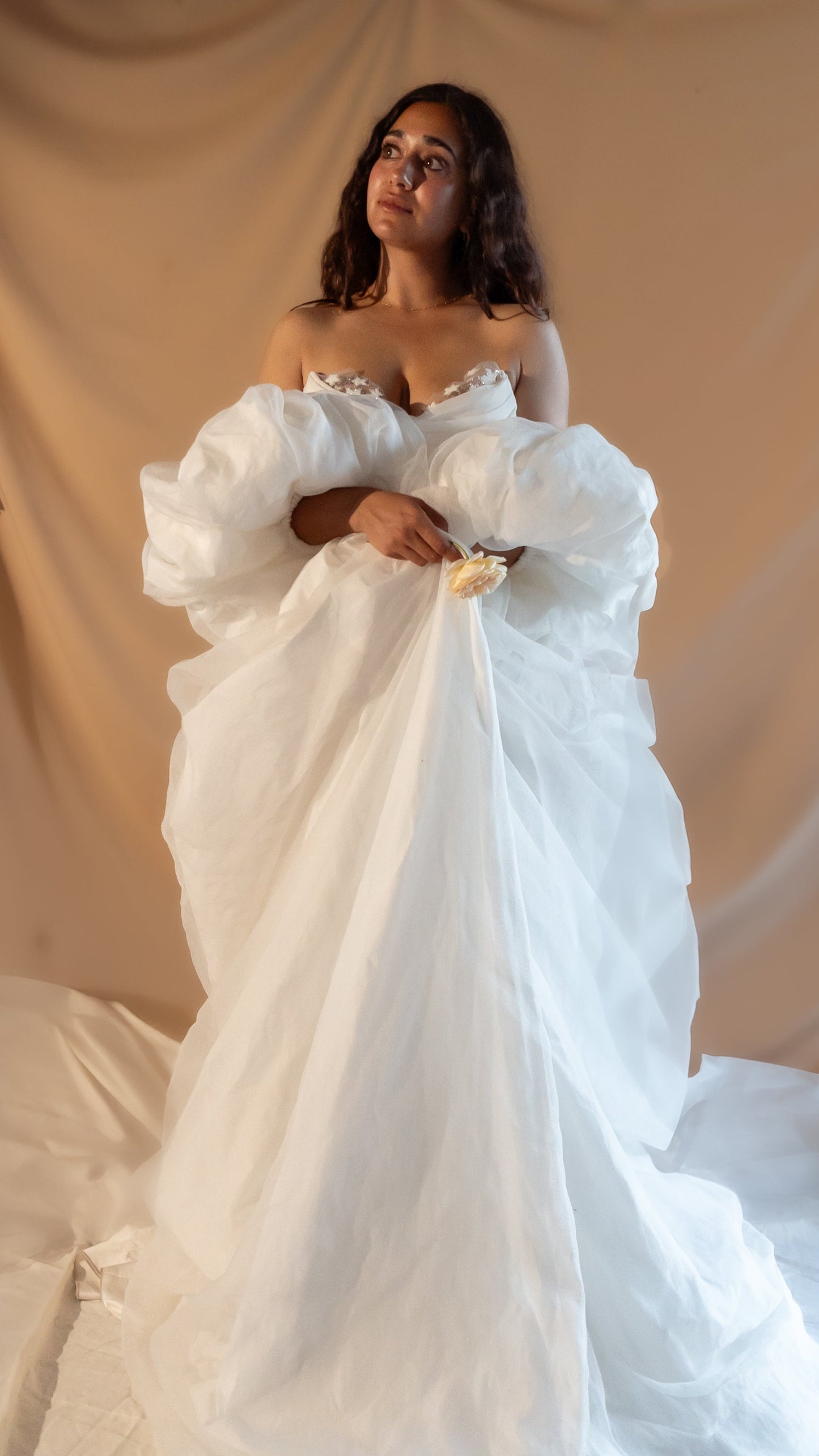 Woman in a fairytale vintage Basque waist wedding dress with a long train and puff sleeve cape with stars against a beige curtain backdrop